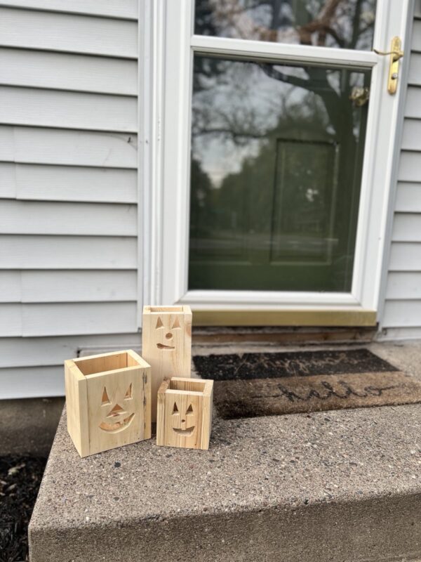 set of three unlit, unfinished wooden jack-o-lantern fall decor luminaries on a front step